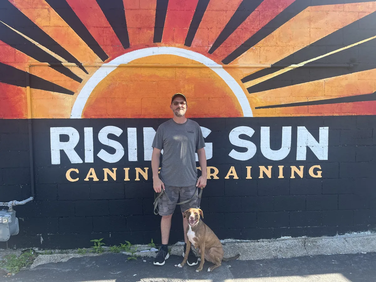 Rising Sun Canine Training trainer with a dog in front of the Rising Sun mural in Marion, IL