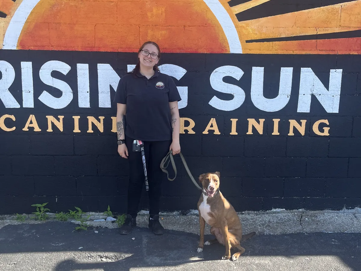 Rising Sun Canine Training trainer with a dog in front of the Rising Sun mural